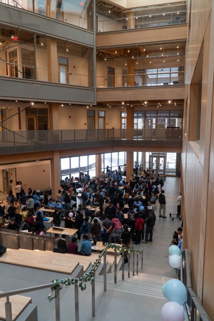 High-angle view of the hackathon atrium filled with teams working at numbered tables.