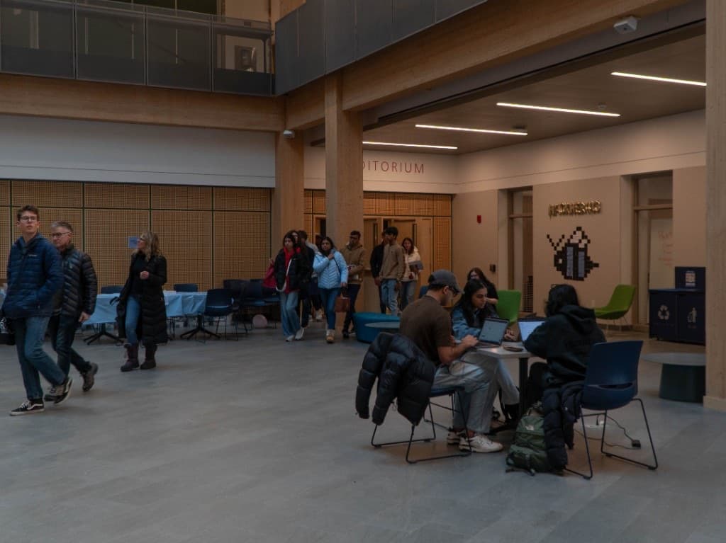 The event lobby with the pixel bee mural, gold HackHer branding, and teams working nearby.